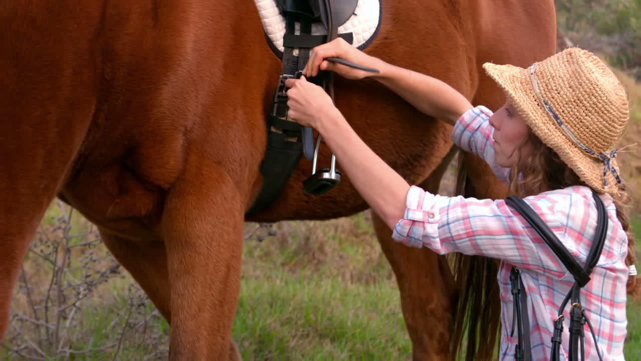 mujer poniendo una silla de montar en un caballo