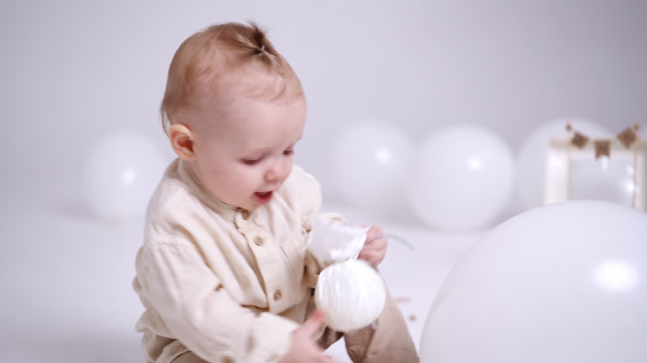 Lovely Caucasian baby wearing beige shirt holding a toy. Kid tries to stand up but drops. Studio footage.