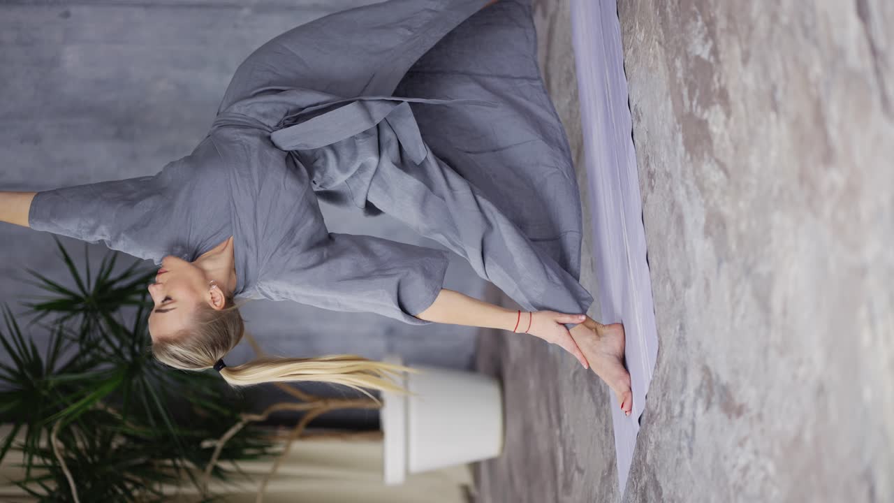 로브를 입은 매력적인 여성 요가 소파가 삼각형 자세를 취하는 우티타 트리코나사나 전사 자세로 전환하는 비라바드라사나