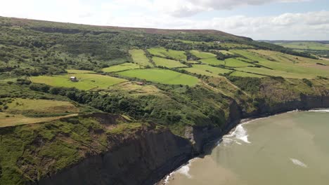 Aerial-drone-shot-of-North-Yorkshire-coastline-near-Ravenscar-with-green-fields-and-ocean