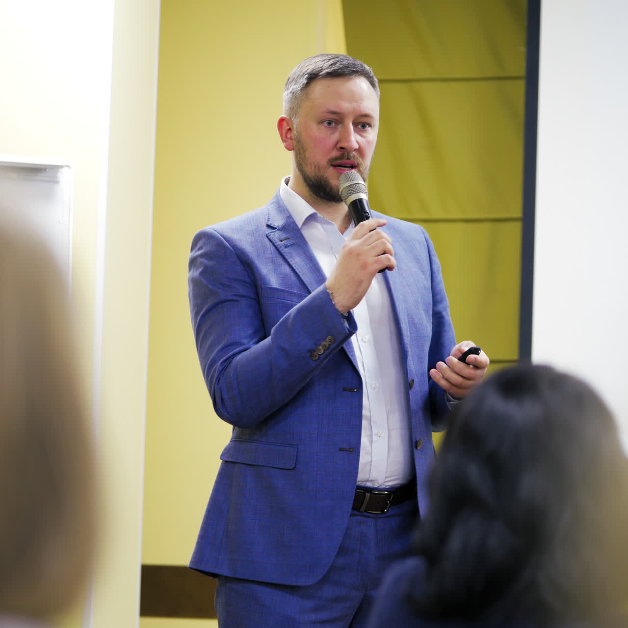 Experienced speaker talking into a microphone. Executive leader in stylish suit conducts a speech to the audience in conference hall.