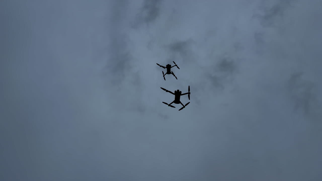 Drones fly above the clouds during an event in the afternoon sky. Two drones are flying in the cloudy sky during the afternoon at a local event