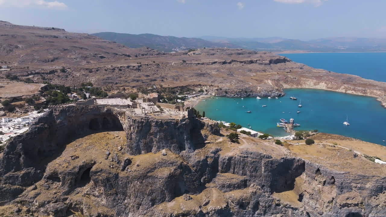 Aerial tracking shot of the Lindos fortress and the Pallas beach, in sunny Rodos
