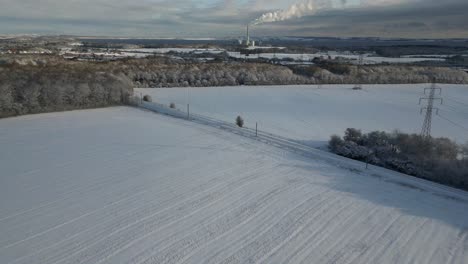 drone footage of snowy fields, with a power plant on the horizon