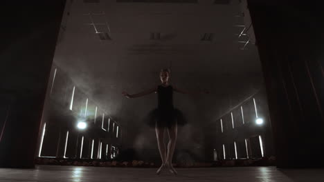 ballerina is practicing her moves in dark studio. young girl dancing with air white dress tutu spinning around and smiling. gracefulness and tenderness in every movement