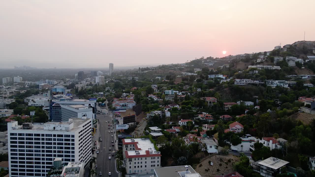 Vista aerea di un tramonto sopra un quartiere collinare, il paesaggio urbano di West Hollywood e lo skyline di Los Angeles sullo sfondo - panoramica, ripresa con drone.
