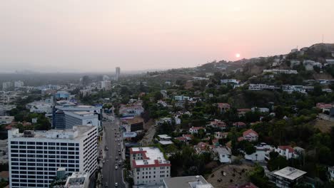 Vista-Aérea-De-Una-Puesta-De-Sol-Sobre-Un-Vecindario-En-La-Ladera,-El-Paisaje-Urbano-Del-Oeste-De-Hollywood-Y-El-Fondo-Del-Horizonte-De-Los-ángeles---Pan,-Tiro-De-Drones