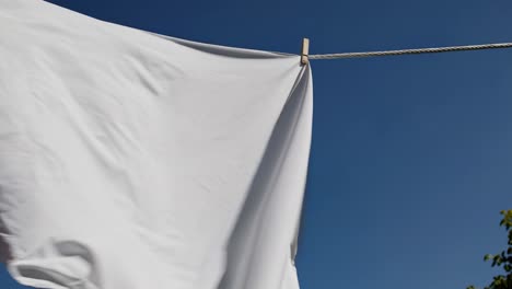 low-angle video shot of a white sheet fluttering on a clothesline against a clear blue sky