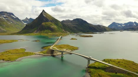 Drone-shot-from-camper-driving-over-bridge-in-Lofoten-Norway-with-mountains-in-the-background