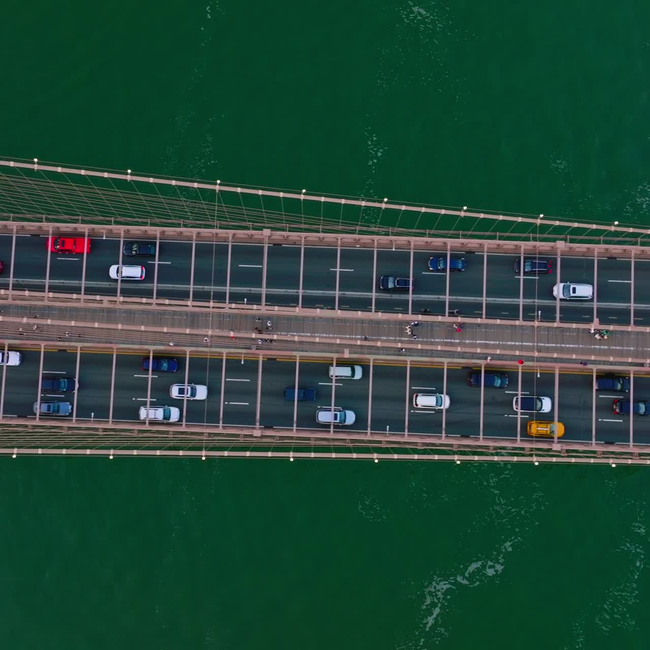 Many cars moving back and forth along the huge bridge over the river. Bird's eye view on the bridge at the backdrop of sea-green water