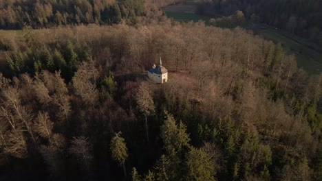 aerial footage of a small chapel on top of a hill that is covered with dry, brown trees