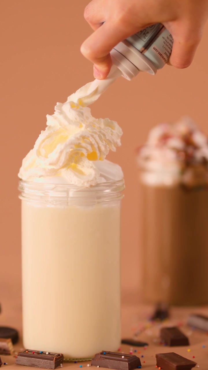 Primo piano di una mano che fa roteare panna montata su un milkshake alla vaniglia, illuminazione calda da studio, telecamera fissa