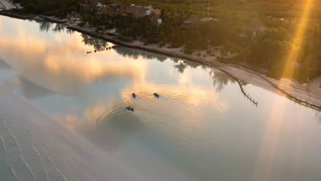 Menschen-Paddeln-Bei-Sonnenuntergang-Mit-Kajaks-Am-Strand-Entlang,-Wolken-Spiegeln-Sich-Im-Meer