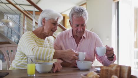 senior caucasian couple pouring milk in cereal bowl having breakfast together at home