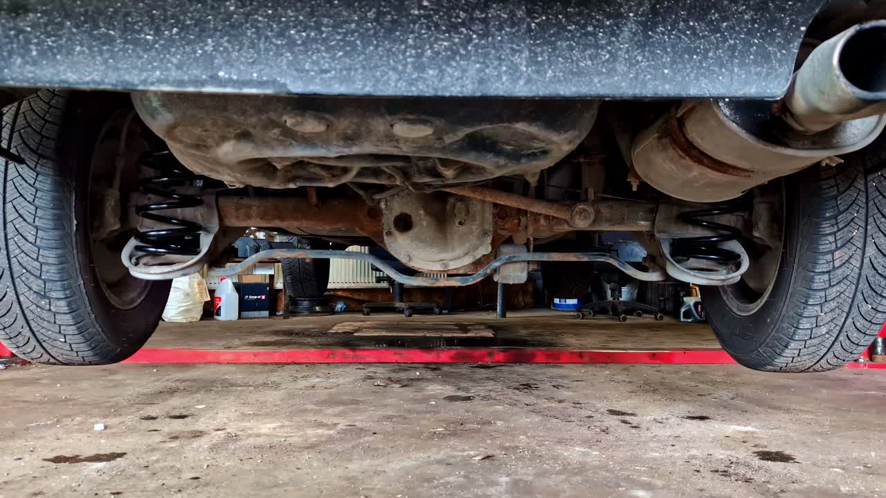 Vue sous une voiture soulevée dans un atelier de réparation avec outils et équipement.