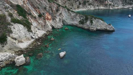 kayak moves in coastal water by seaside cliffs at gjipe, albania, forward aerial
