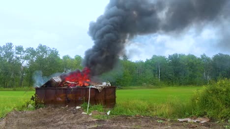 thick dark smoke billowing from a burning dumpster full of garbage on rural farmland