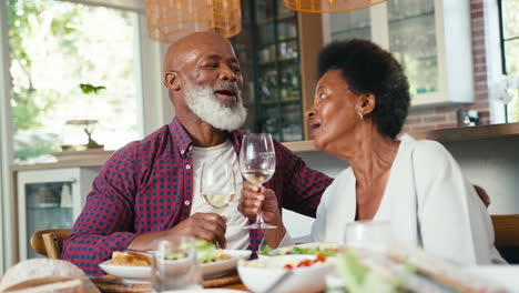 Amorosa-Pareja-De-Ancianos-Sentados-Alrededor-De-La-Mesa-En-Casa-Disfrutando-De-Una-Comida-Con-Vino-Juntos