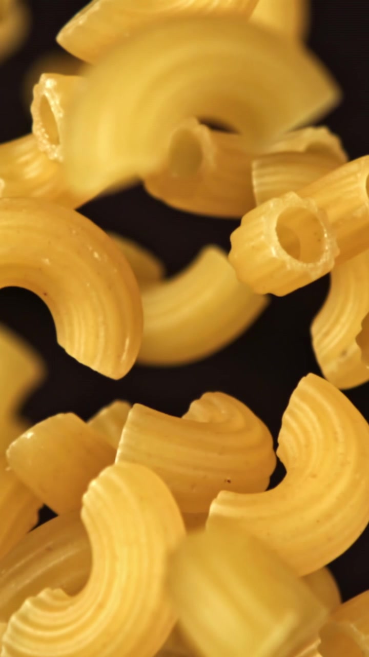 Primo piano di pasta maccheroni secca in caduta su sfondo scuro