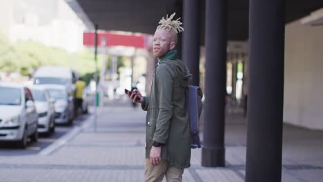 thoughtful albino african american man with dreadlocks walking on street using smartphone