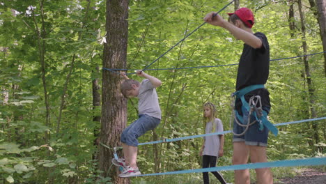 children on a summer camp hike are moving along the ropes with the help of a guide who teaches children rock climbing and tourism. a boy in the forest overcomes a rope barrier