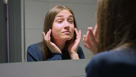 mujer joven mirando a un espejo del baño, chequeando la piel y el cabello, en cámara lenta
