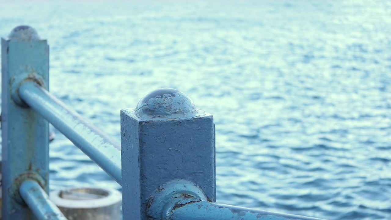 Close-up of blue metal railing on a pier overlooking the ocean