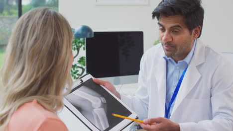 Médico-Con-Bata-Blanca-En-El-Consultorio-Con-Una-Paciente-Madura-Mirando-Una-Radiografía-O-Exploración-Médica