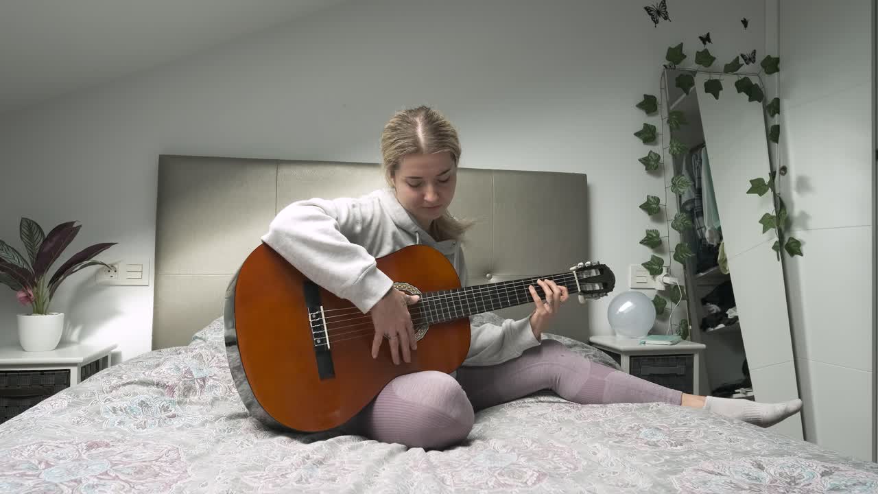 Young woman strumming an acoustic guitar while relaxing on her bed