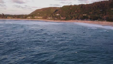 A-beautiful-aerial-view-of-the-North-Shore-beach-at-sunrise,-highlighting-the-soft-waves-and-lush-greenery-along-the-coastline