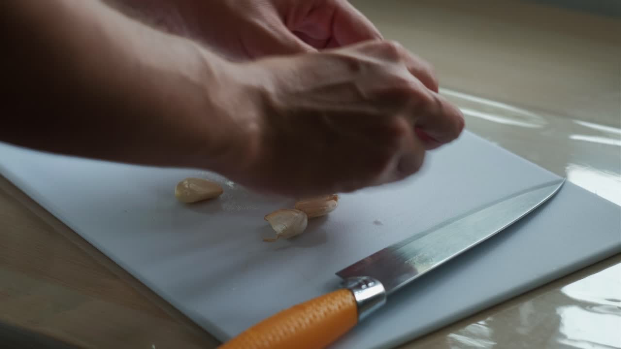 Close-up shot of hands peeling and removing garlic cloves for mincing.