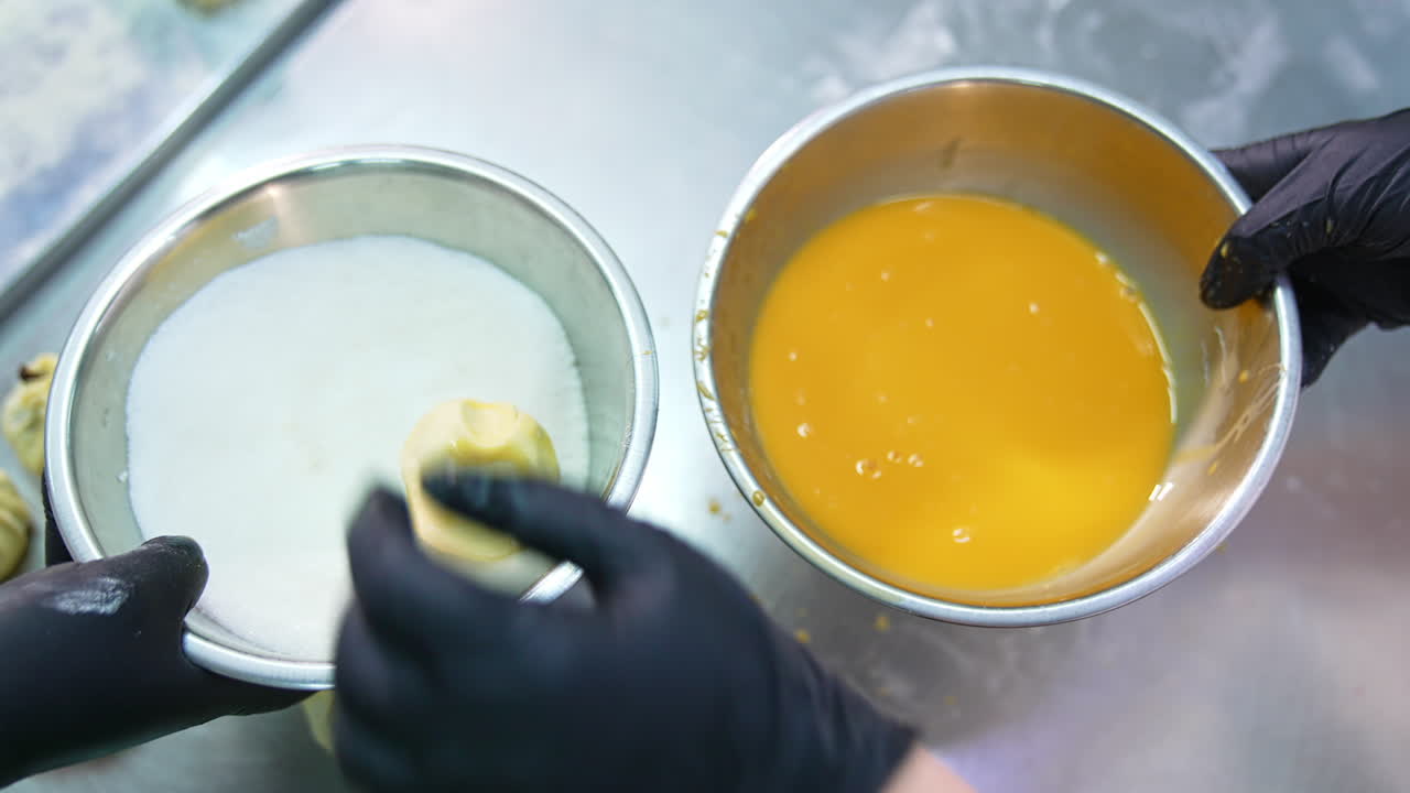Sweet desserts production at confectionary factory. Handmade desserts coated with egg and sprinkling. Close up.