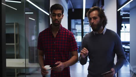 Asian-businesswoman-walking-using-smartphone-holding-cup-of-coffee-in-modern-office