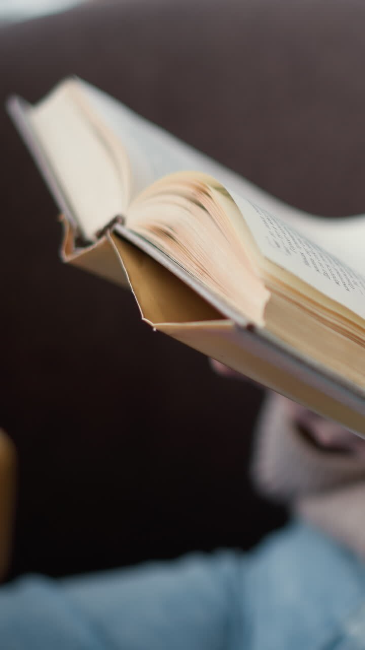Primo piano di una giovane donna seduta comodamente che sfoglia le pagine del suo libro, intenta a leggere. Gira la pagina successiva mentre è immersa nel contenuto.