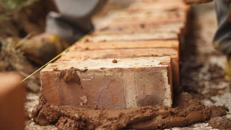 close up of hand laying down brick in wall with brown cement mixture