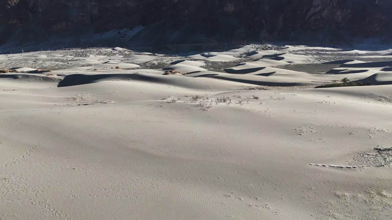 Aerial drone shot showcasing the textured patterns of Nubra Valley's dunes under soft sunlight and clear skies.