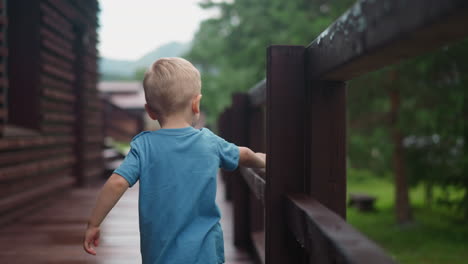 curious little boy touches wet wooden railing on deck