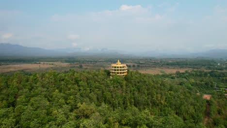 aerial drone flying low over a dense forest towards a golden wat doi sapanyoo in the mountain hills of chiang mai thailand on a sunny summer day