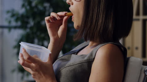 vista de cerca de una mujer embarazada con anteojos sentada en la oficina y comiendo fruta seca saludable mientras acaricia su vientre