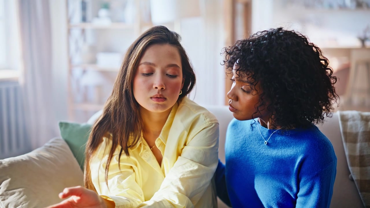 Distressed woman covering face, friend consoles her. Emotional support talk