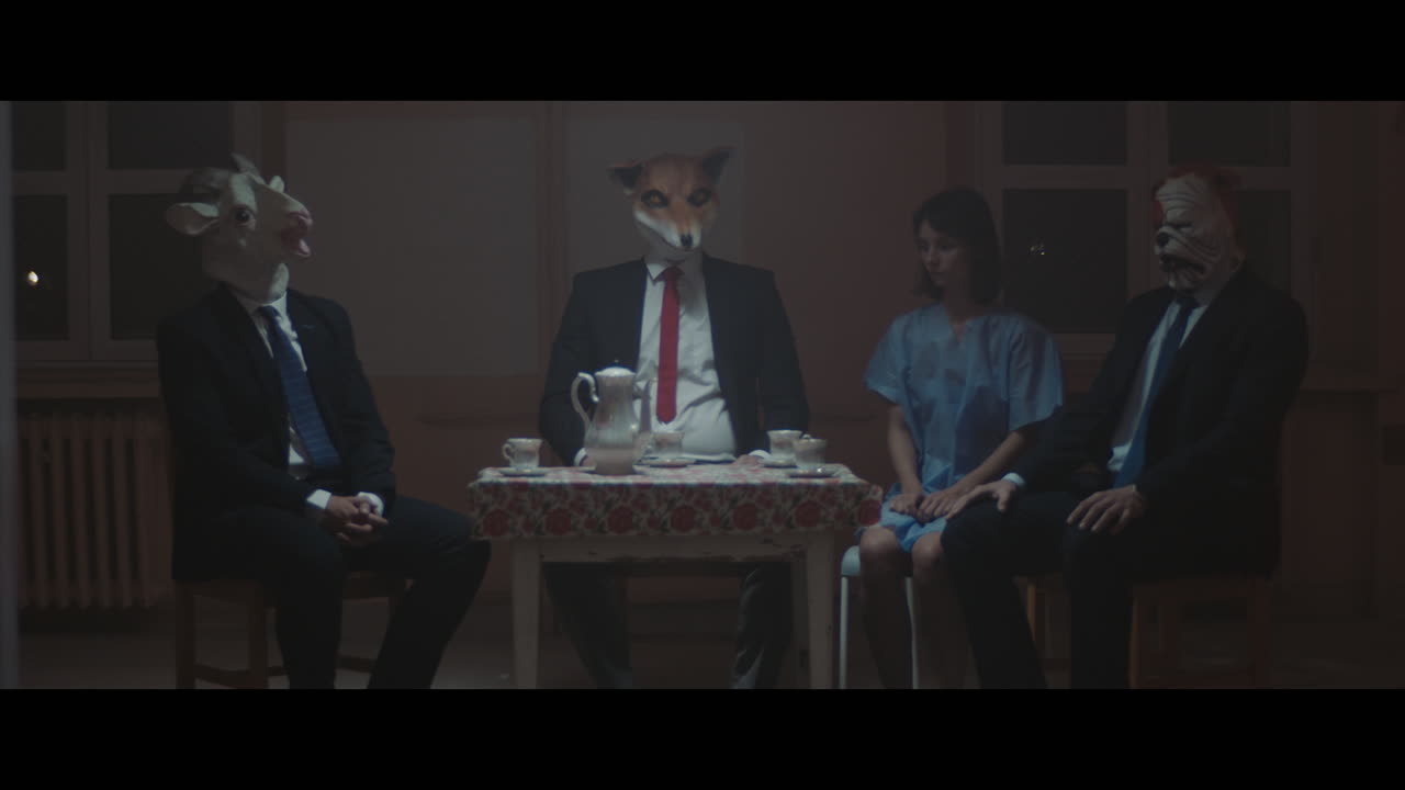 A girl sits at a table with strange figures in animal masks