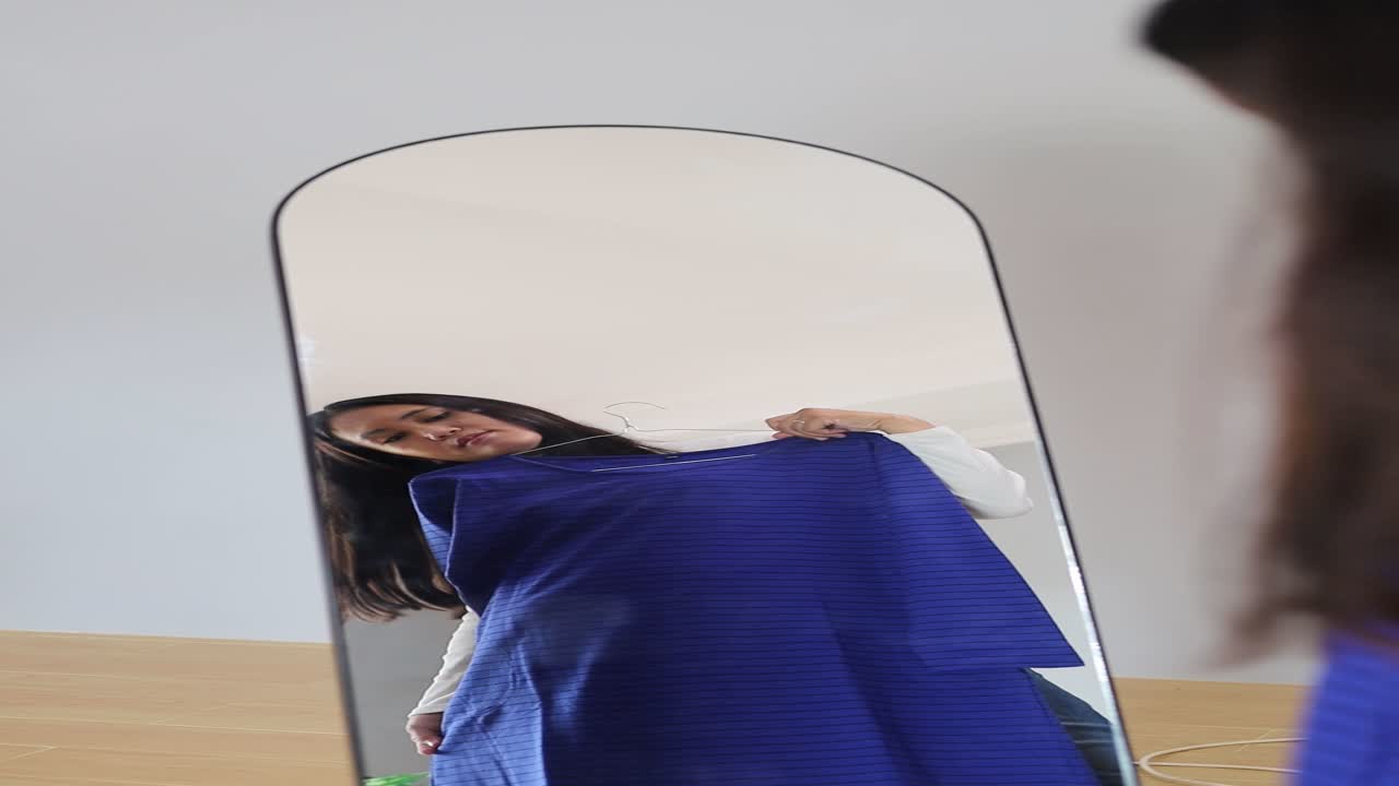 Giovane donna asiatica sceglie l'abito femminile perfetto per un appuntamento, guardando il suo riflesso nello specchio.