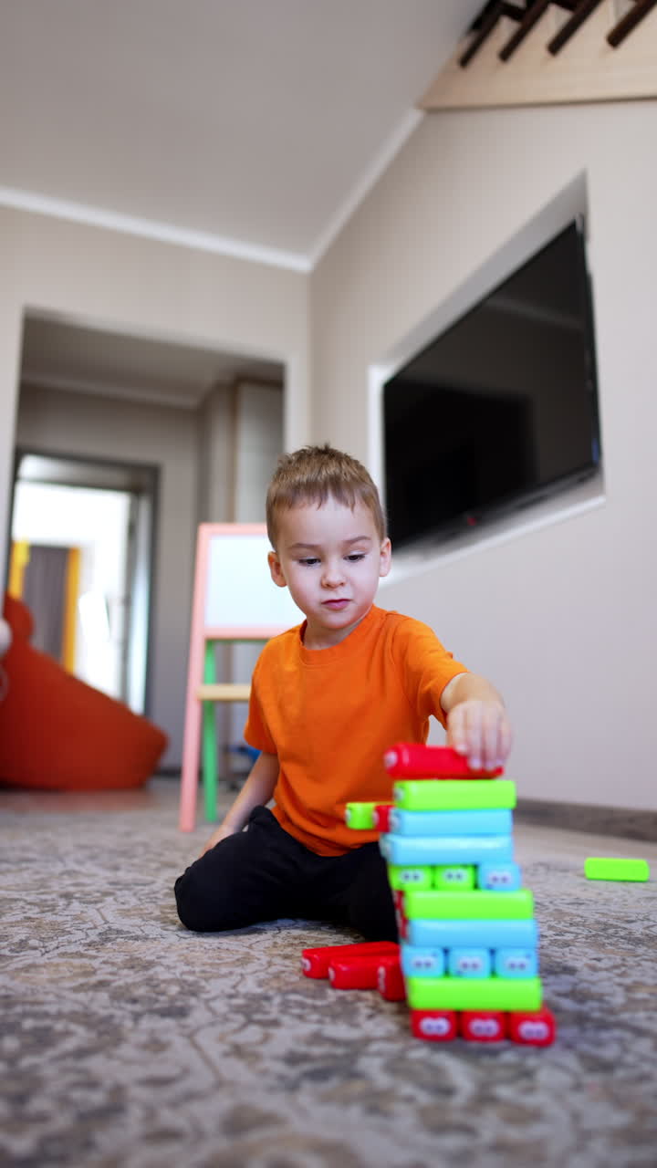 Cute toddler boy building a tower. Cute kid puts bricks on a pile and watches them fall. Vertical video.