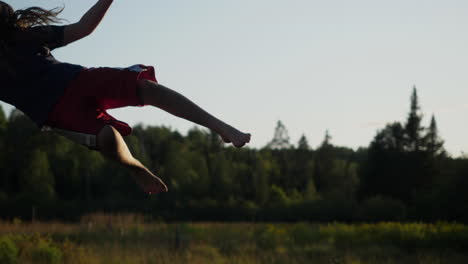 Camera-pan-of-a-kid-jumping-and-flailing-around-in-front-of-barn-and-field