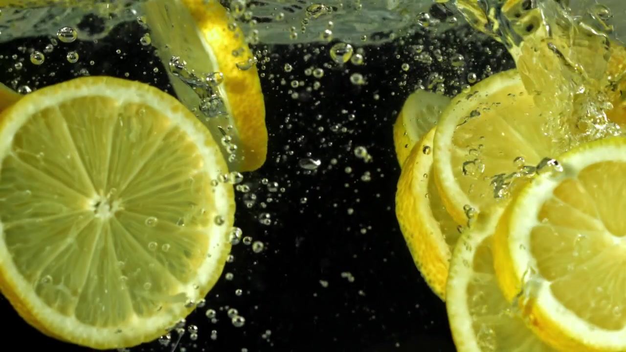 Fette di limone fresche che schizzano nell'acqua al rallentatore.