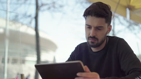 Doubtful man using digital tablet in outdoor cafe
