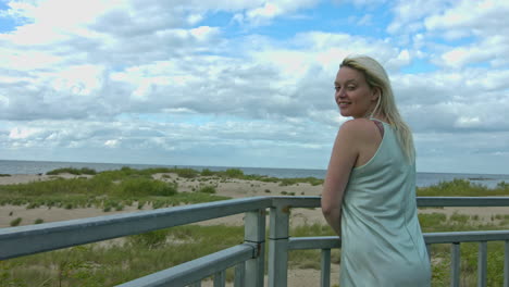 Blonde-girl-in-tank-top-standing-and-smiling-on-terrace