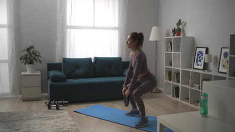 training with weights at home young sportswoman is doing squats with weight in hands working muscles of buttocks and legs sporty sexy lady in modern apartment