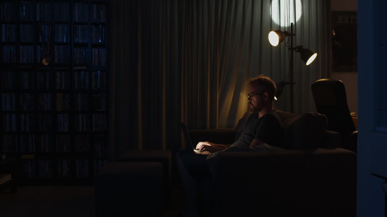 Workaholic man working on a laptop in his living room late at night