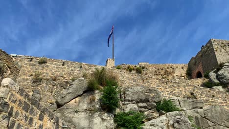 Vista-Inferior-De-La-Bandera-De-Croacia-Ondeando-En-La-Antigua-Fortaleza-De-Klis,-Famoso-Lugar-De-Rodaje-Del-Juego-De-Tronos